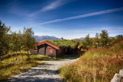 a small building with a grass roof on a dirt road at Stor tømmerhytte med fjellutsikt in Beitostøl