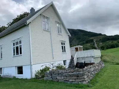 a white house with a stone wall in front of it at Flø Feriehus med Badstue in Ulstein