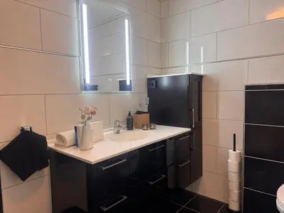 a bathroom with a sink and a black refrigerator at Modern apartment, large terrace free parking and Wallbox in Ytterland