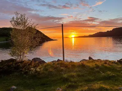 a sunset over a body of water with a pole at Flott feriehus ved sjøen