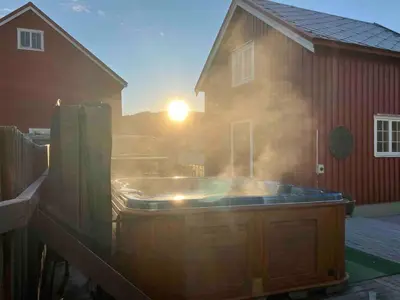 a hot tub in front of a house with the sun setting at Gårdsleilighet in Verdal
