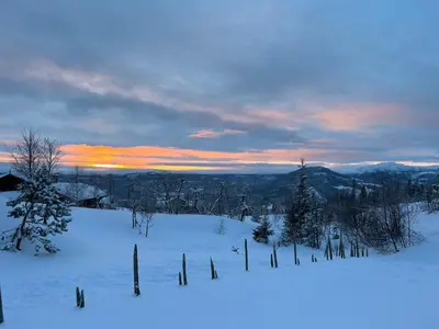 a snow covered field with trees and a sunset at Sleepover in the mountains in Hjartdal