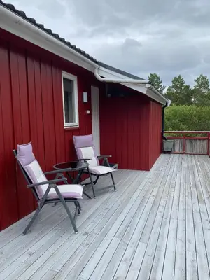 two chairs and a table on a deck with a red building at Bjørnafjorden