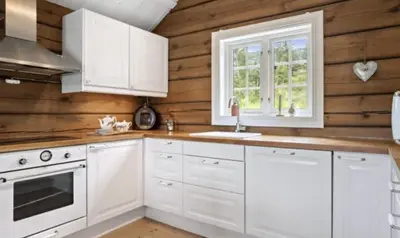 a kitchen with white cabinets and wooden walls at Timber Cabin With Soul At Kvamskogen in Norheimsund