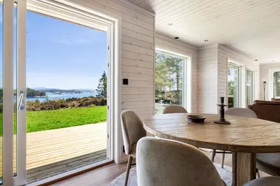 a dining room with a wooden table and a large sliding glass door at Ny feriehytte i skjærgården in Austevoll