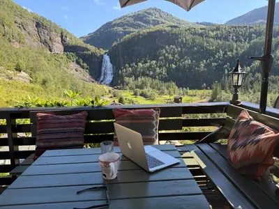 a laptop sitting on a wooden table with a view of a waterfall at Fossen Bratte Mountain home in Eikedalen