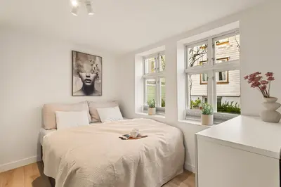 a white bedroom with a bed and two windows at Historisk hus fra 1800-tallet in Bergen