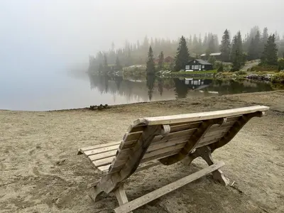 a wooden bench sitting on a field next to a lake at Newly Renovated Cabin By Sjusjoen Ski Slopes in Sjusjøen