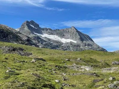 a mountain range with a green field with snow at Harevadet 217 in Volda