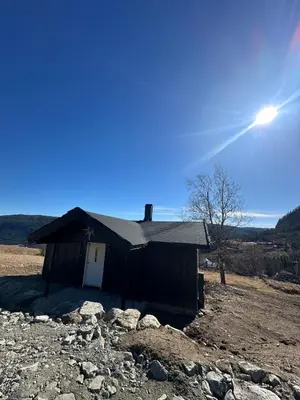 a small house in a field with the sun behind it at Cozy little cottage for rent in Oppheim in Ål