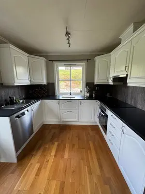 a kitchen with white cabinets and a wooden floor at 75 sqm with terrace and garden in Elverum