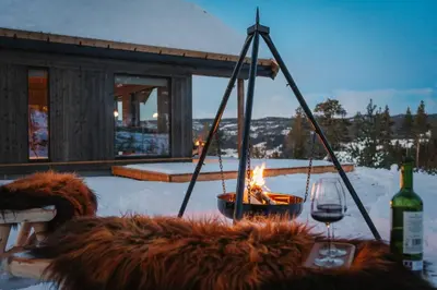 a fire pit with a bottle of wine and a glass at Tiur, stylish new cabin with hot tub in Nesbyen