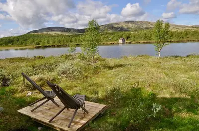 two benches sitting on a wooden platform next to a lake at Fiskebu at Flaksjøen in Venabygd