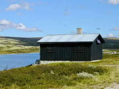 a black building sitting on top of a hill next to a lake at Hyggelig fiskebu ved Langrumpa fiskevann in Venabygd