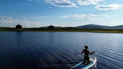 a man on a paddle board in the water at Hyggelig fiskebu ved Langrumpa fiskevann in Venabygd