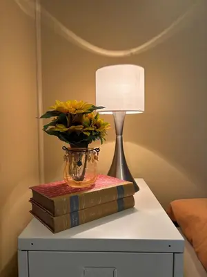 a lamp on a table with books and a vase with flowers at 3 soveroms leilighet-komfort og stil -perfekt for ferie og jobb in Gjøvik
