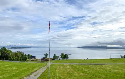 a flag on a pole in a field next to a lake at Lovely Home In Fiksdalen in Fiksdal