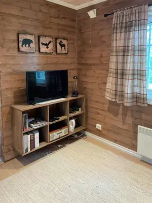 a living room with a television on a wooden wall at Traditional Log Cabin By Lake Mykletjønn in Austbygdi