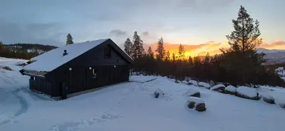 a small cabin in the snow with the sunset in the background at Elegantes, ruhiges Ferienhaus in bester Lage für alle Outdoorfans in Randsverk