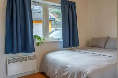 a bedroom with a bed with blue curtains and a window at Small house close to nature and city in Bergen