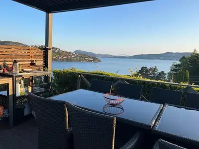 a table and chairs on a deck with a view of the water at Villa med 5 soverom, 4 bad og 3 kjøkken, 400 m fra lokal badestrand in Bergen