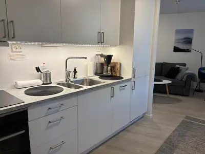 a kitchen with white cabinets and a sink and a living room at Modern Apt - Steps from Grieghallen and Trainstation in Bergen