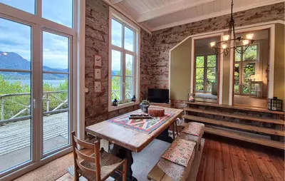 a dining room with a table and some windows at Beach Front Home In Vaksdal With House Sea View in Vaksdal