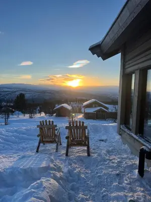 two wooden chairs sitting on a snow covered porch with the sunset at Exclusive cottage on Geilo in Hol