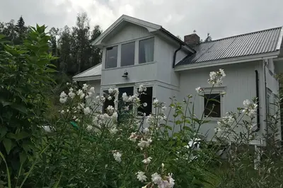 a white house with flowers in front of it at Cosy farmhouse with spa as add on service in Gjøvik