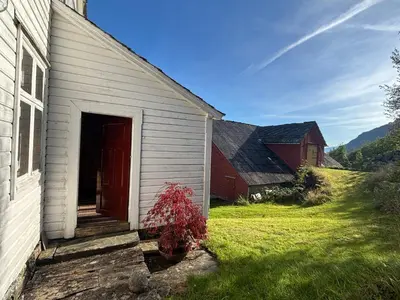 a white building with a red door and a yard at Jåstad Gjestetun in Jåstad