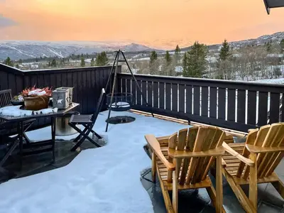 a patio with a table and chairs on a deck with snow at Panoramic Apartment In The Heart Of Beitostølen in Beitostøl