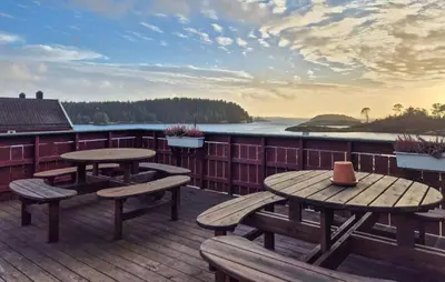 two picnic tables and benches on a deck overlooking the water at Beautiful Home In Bøvågen With Sauna in Bøvågen