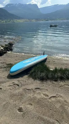 a blue surfboard sitting on the beach next to the water at Casa Hauge - Fjord View in Sandane