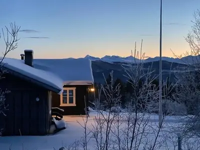 a house covered in snow with mountains in the background at Historic Timber Cabin With Views Of Rondane in Furuhovde