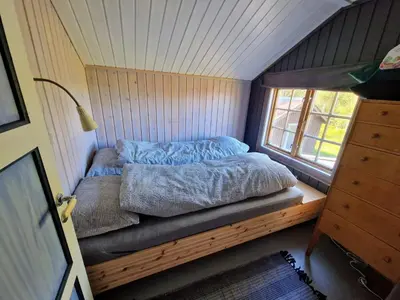 a bed in a tiny house with a window at Trivelig og romslig hytte nær Røros, rikelig med uteplass in Glåmos