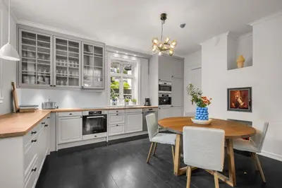 a kitchen with white cabinets and a wooden table and chairs at Elegant Historic Villa - Stunning Views in Bergen