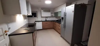 a kitchen with a black refrigerator and wooden cabinets at Rooms in easy accessible new apartment near Stave church in Bergen