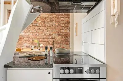 a kitchen with white cabinets and a brick wall at Koselig bygårdsleilighet i Bergen sentrum in Bergen
