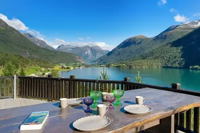 a table with plates and wine glasses on a balcony overlooking a lake at Luxury cabin with amazing views in Stryn