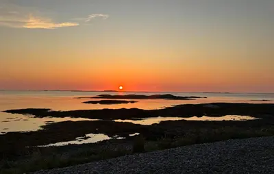 a sunset over the ocean with rocks in the water at Nice Home In Harøya With Harbor View in Steinshamn