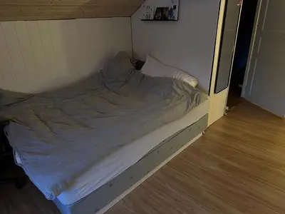 an unmade bed in a room with a wooden floor at Bolig sentralt på Røros in Røros