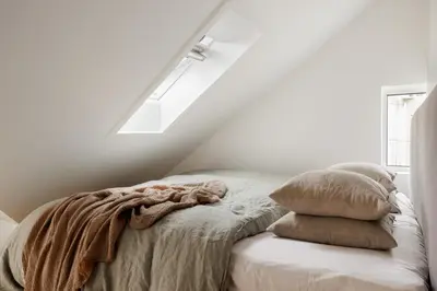 a bed with a blanket and pillows in a white room at Relaxed apartment with a view in Bergen