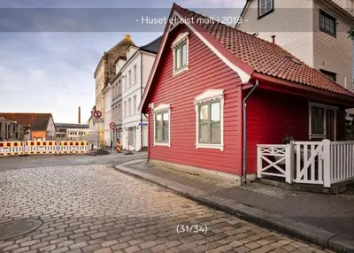 a red house with a white fence next to a street at Sentralt,unikt lite bergenshus med sjel på fine Nøstet! in Bergen