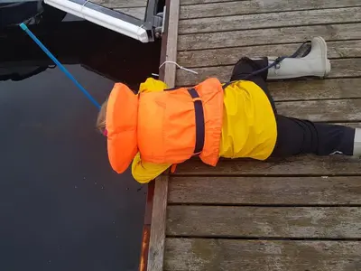 a person in an orange and yellow life vest sitting on a dock at Holiday home Hemnskjel in Hitra