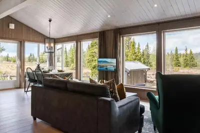 a living room with a couch and chairs and windows at Solglimt, mountain cabin in Golsfjellet with jacuzzi in Gol