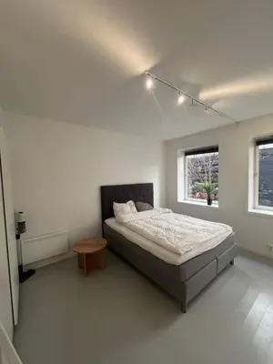 a bedroom with a bed and a table and two windows at Nice and central apartment in Sandviken with sea view in Bergen