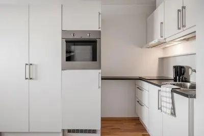 a white kitchen with white cabinets and a sink at Riverside studioapartment 100m from trainstation! in Trondheim