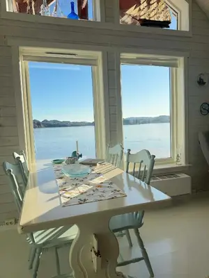 a table and chairs in a room with two windows at Cabin by the lake in Sveio