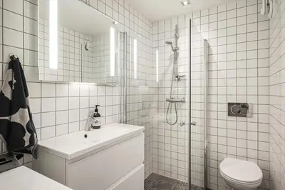 a white tiled bathroom with a shower and a toilet at Stylish 2BR with Patio and Smart TV - 10 min to Bryggen in Bergen
