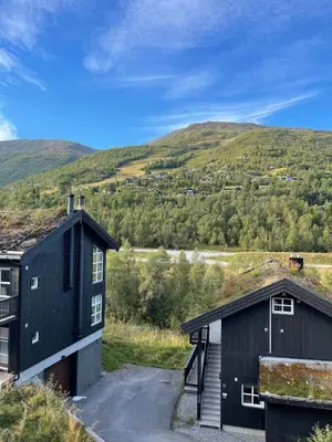 two black buildings with a mountain in the background at Velkommen til topp leilighet på Strandafjellet 2 soverom og hems in Stranda